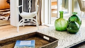 A modern living room with a white chair, a wicker tray with a book, and green vases on a speckled floor.
