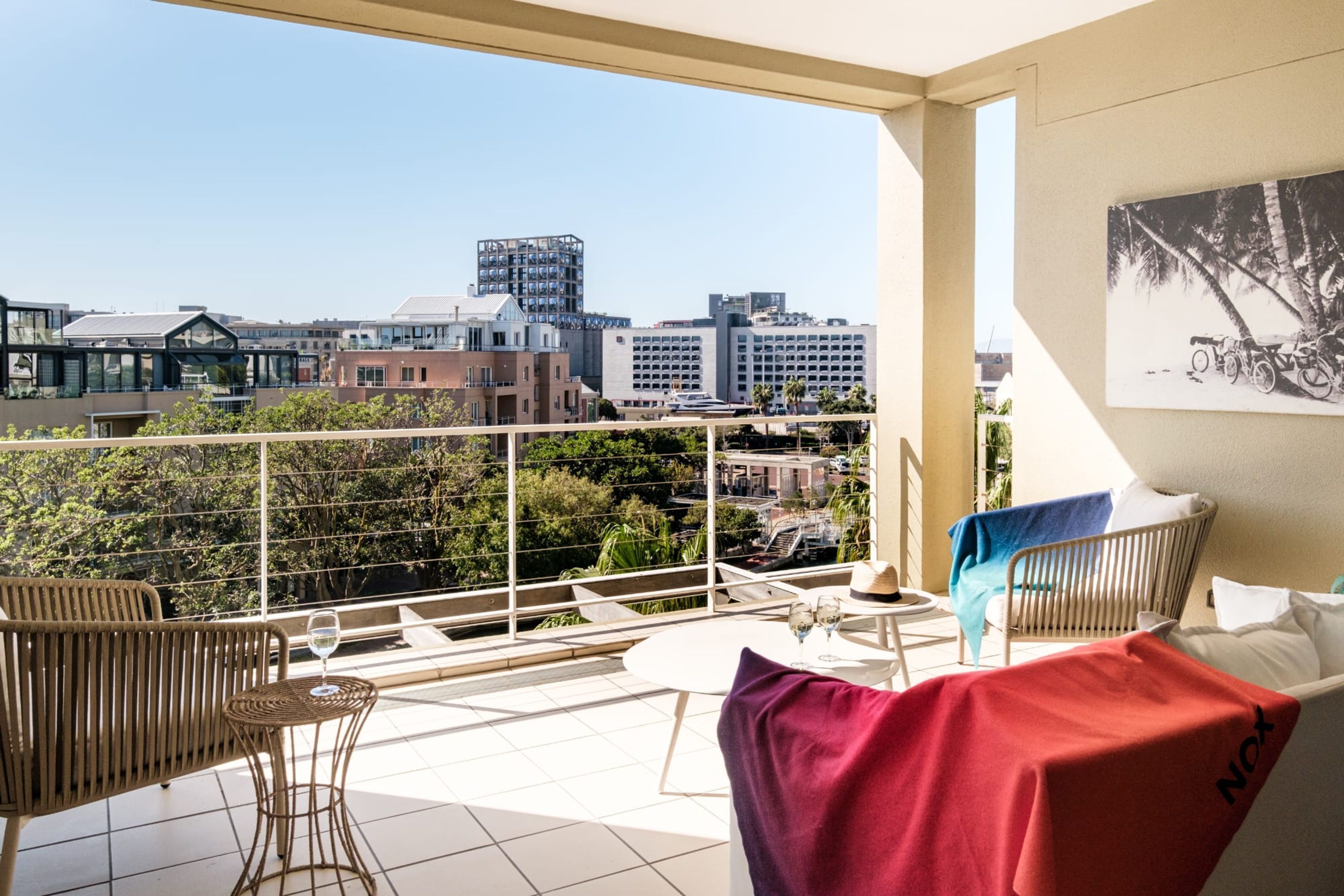 A balcony with a city view, wicker furniture, and a table with wine glasses.
