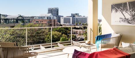 A balcony with a city view, wicker furniture, and a table with wine glasses.