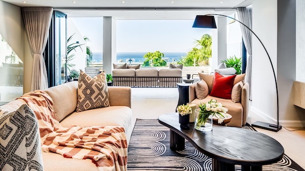 A modern living room with a sofa, coffee table, and a view of the ocean. - Luxurious Villa w Sea City Views Splendor Views (Cape Town)