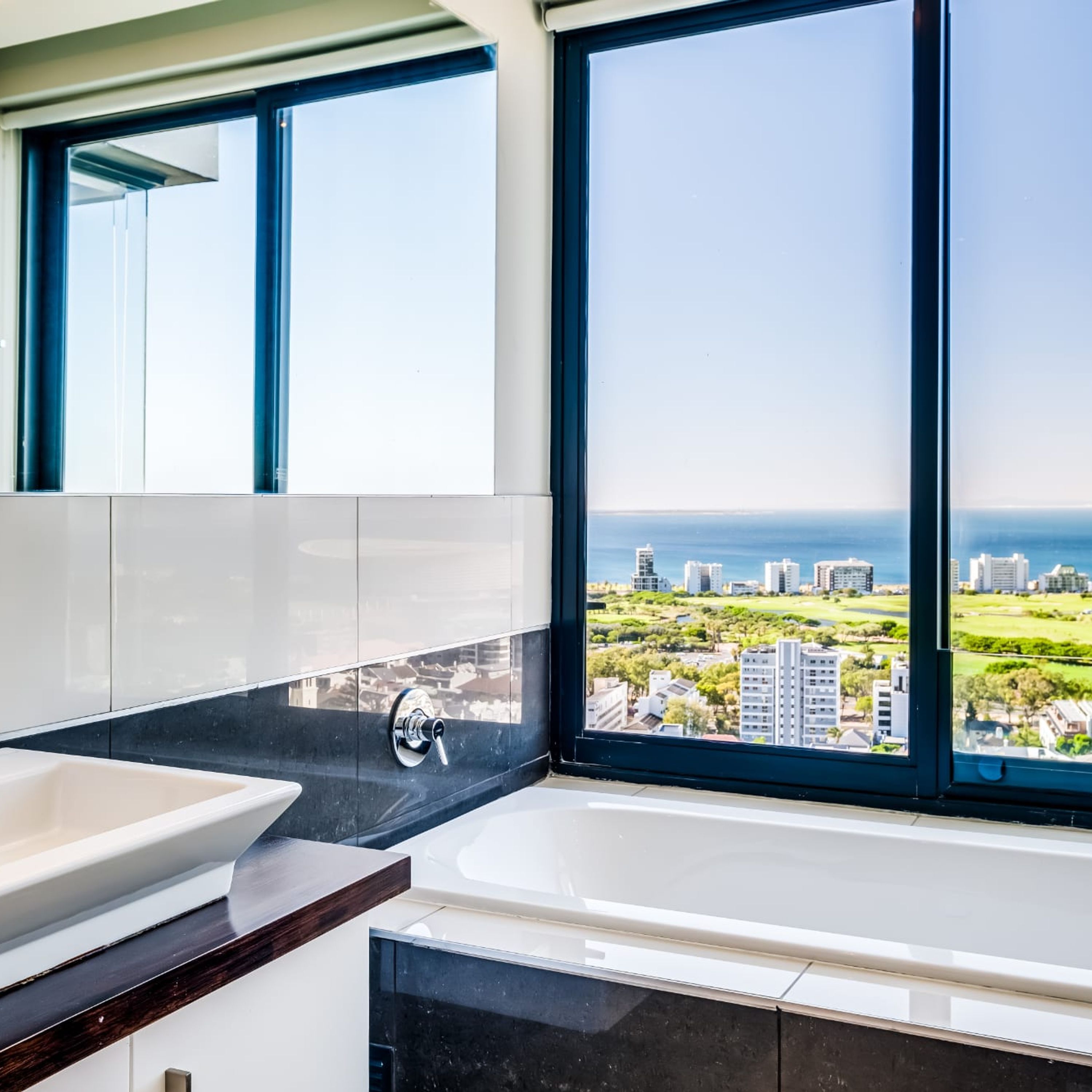A modern bathroom with a large bathtub, a sink, and a window offering a city view.