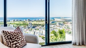 A modern room with a large window offering a city view, a sofa with patterned cushions, and a view of the ocean and distant buildings. - Luxurious Villa w Sea City Views Splendor Views (Cape Town)