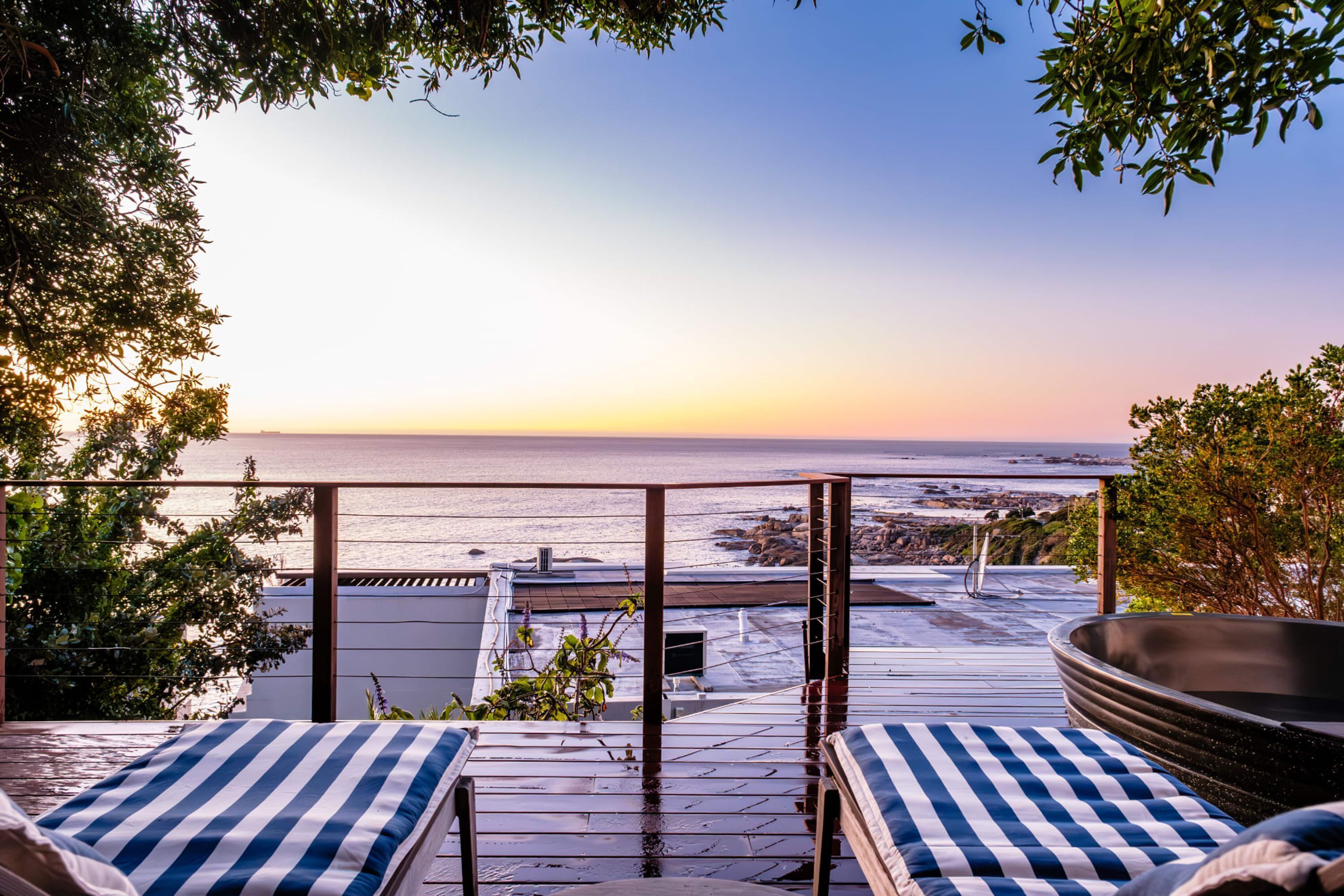 A rooftop terrace with a view of the sea, featuring two striped lounge chairs and a large black bathtub.