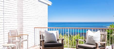 A wooden deck with two chairs and a table, overlooking a clear blue ocean.