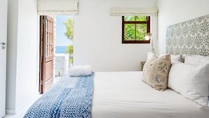 A bedroom with a bed, a nightstand, a window with a view, and a door leading outside. - Luxurious Camps Bay Retreat w Sea Views Rock Residence (Cape Town)