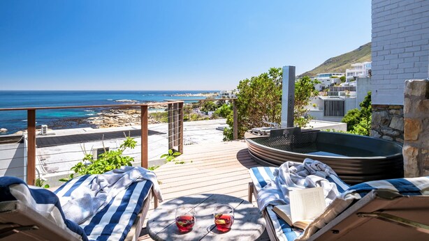 A balcony with two lounge chairs, a hot tub, and a view of the beach and ocean. - Luxurious Camps Bay Retreat w Sea Views Rock Residence (Cape Town)