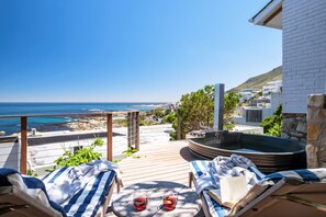 A balcony with two lounge chairs, a hot tub, and a view of the beach and ocean. - Luxurious Camps Bay Retreat w Sea Views Rock Residence (Cape Town)