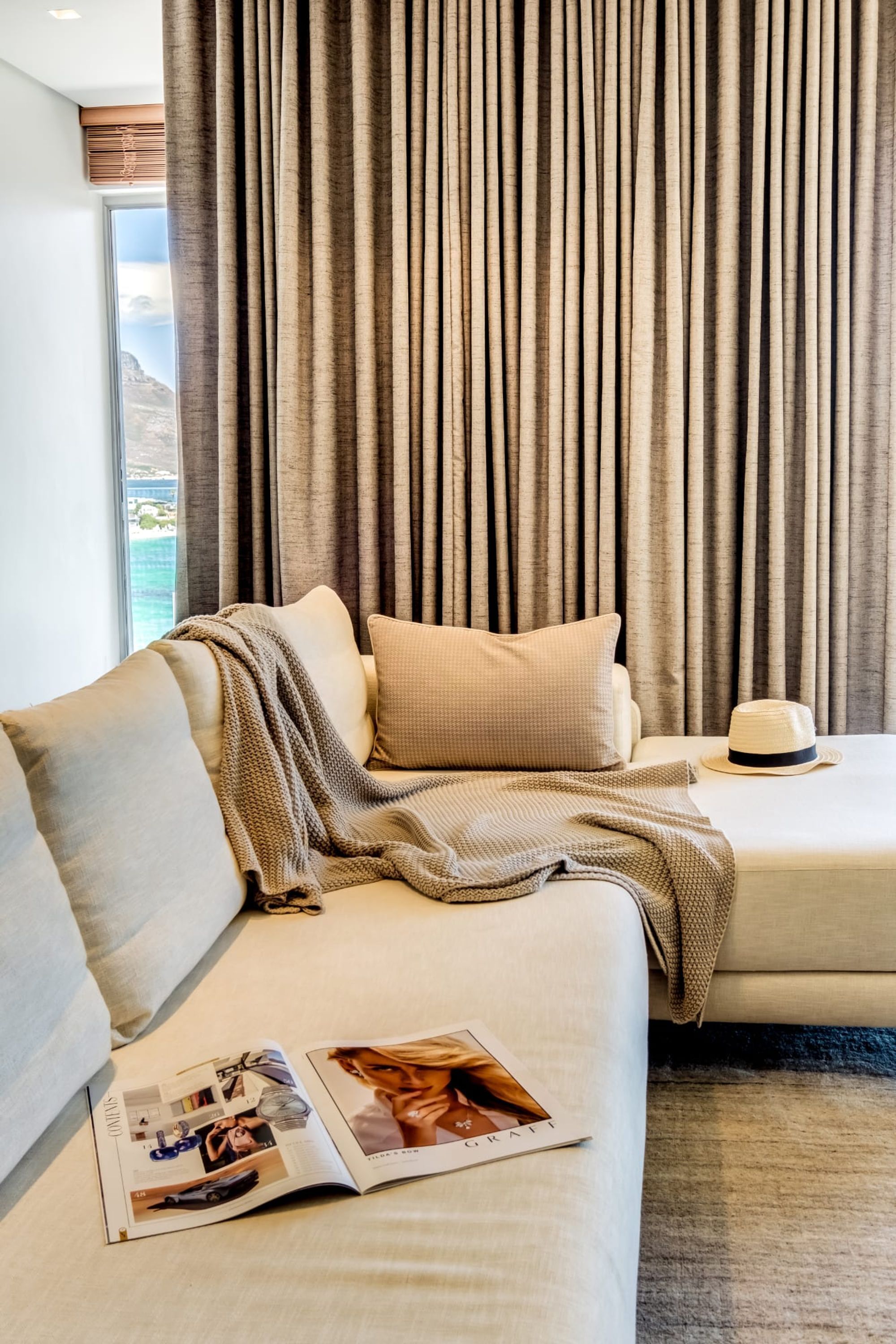 Une chambre d’hôtel avec un canapé et un lit, tous deux dotés de linge de lit beige. Un magazine est posé sur le canapé.