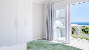 A bedroom with a bed, a wardrobe, and a large window with a view of the sea. - Elegant Apartment w Ocean Views Quenera Apartment (Cape Town)