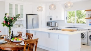 A modern kitchen with white cabinetry, stainless steel appliances, a central island, and pendant lighting. - Elegant Apartment w Ocean Views Quenera Apartment (Cape Town)