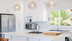 A modern kitchen with white cabinetry, a stainless steel refrigerator, a microwave, a gas stove, and a built-in washing machine. - Elegant Apartment w Ocean Views Quenera Apartment (Cape Town)