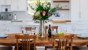 A modern kitchen with white cabinets, a central island, and pendant lighting. - Elegant Apartment w Ocean Views Quenera Apartment (Cape Town)