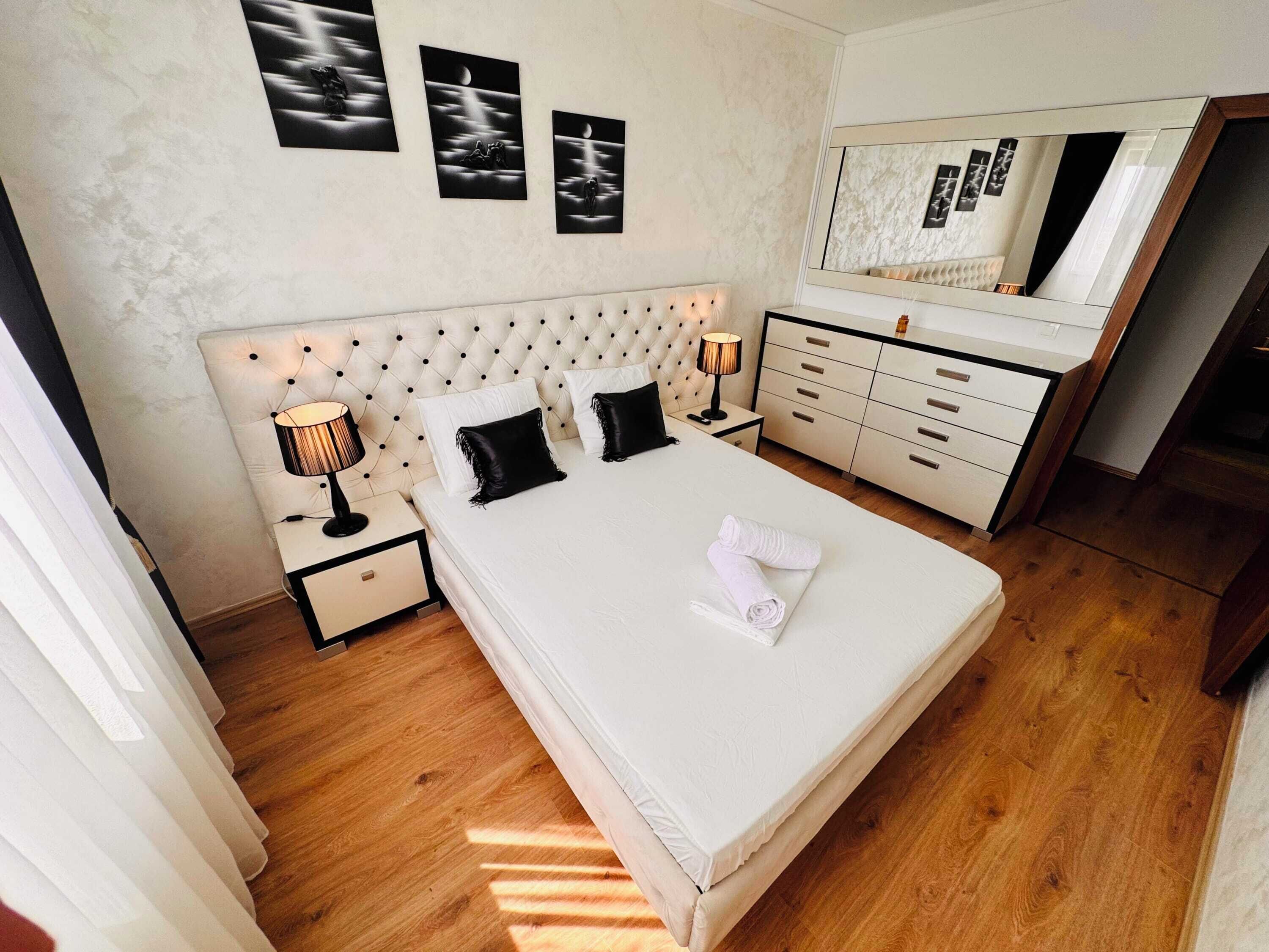 Une chambre à coucher avec une tête de lit capitonnée, un grand lit, une table de chevet avec une lampe, une commode et un miroir.