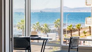 Una habitación con un ventanal grande que da a una playa, una mesa con sillas y un sombrero sobre la mesa.