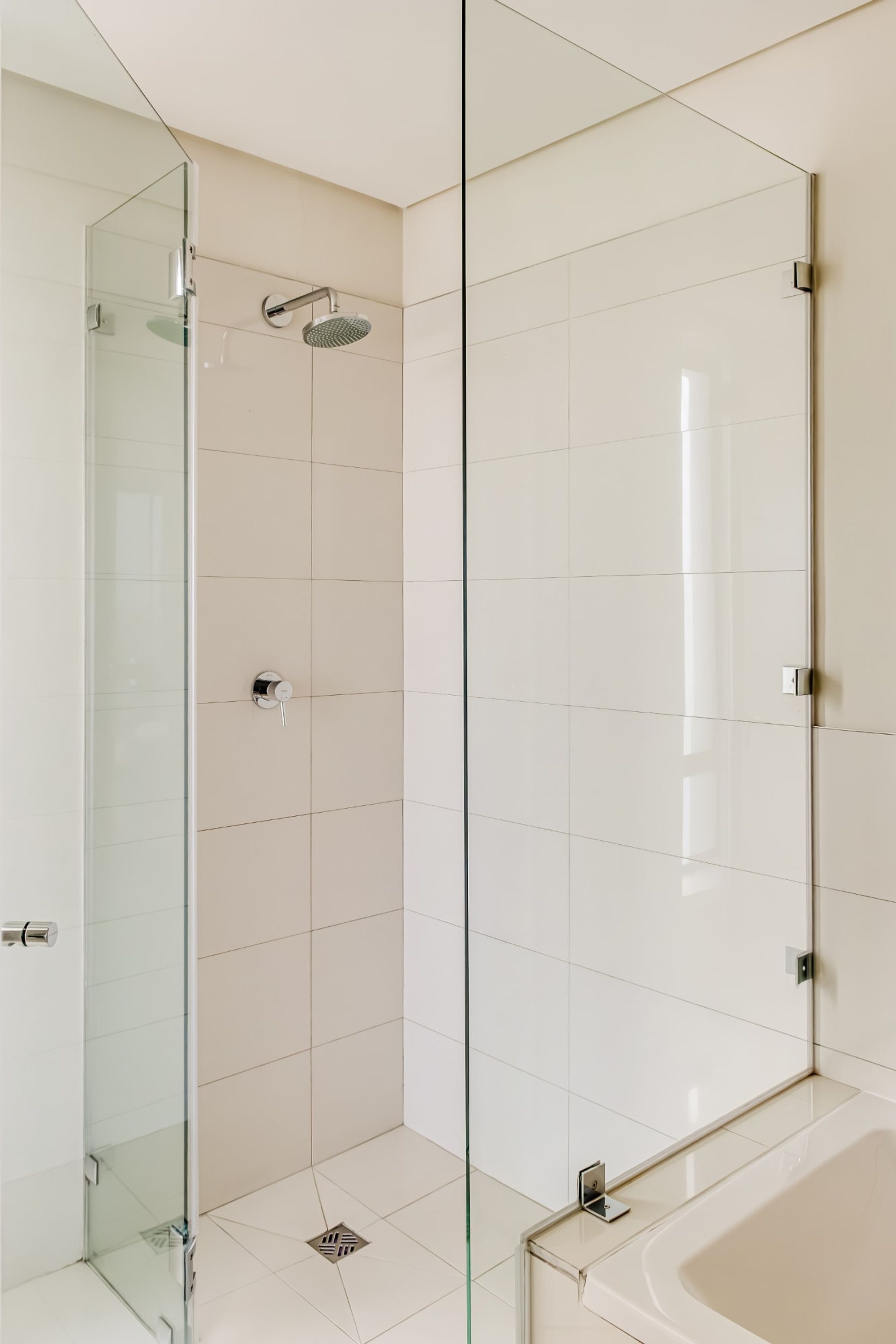 A modern bathroom with a glass-enclosed shower, a standalone bathtub, and white tiled walls.