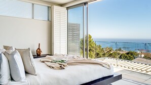 A bedroom with a large bed, a nightstand, and a view of the ocean. - Sea View Sanctuary at Shakawe Villa (Cape Town)