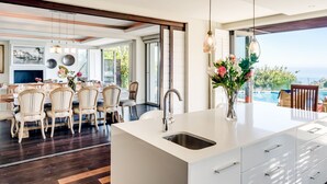 Una cucina moderna con una grande isola, un'area pranzo con sedie e vista sul mare.