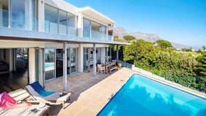 Una casa moderna con piscina, ampie finestre e vista sulle montagne.