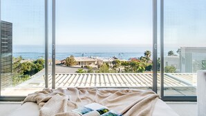 Una camera da letto con un'ampia porta scorrevole in vetro che dà su un balcone con vista sul mare e sugli edifici circostanti.