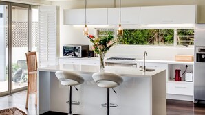 Una cucina moderna con isola centrale, sgabelli da bar, lampade a sospensione e vista su spazi verdi.