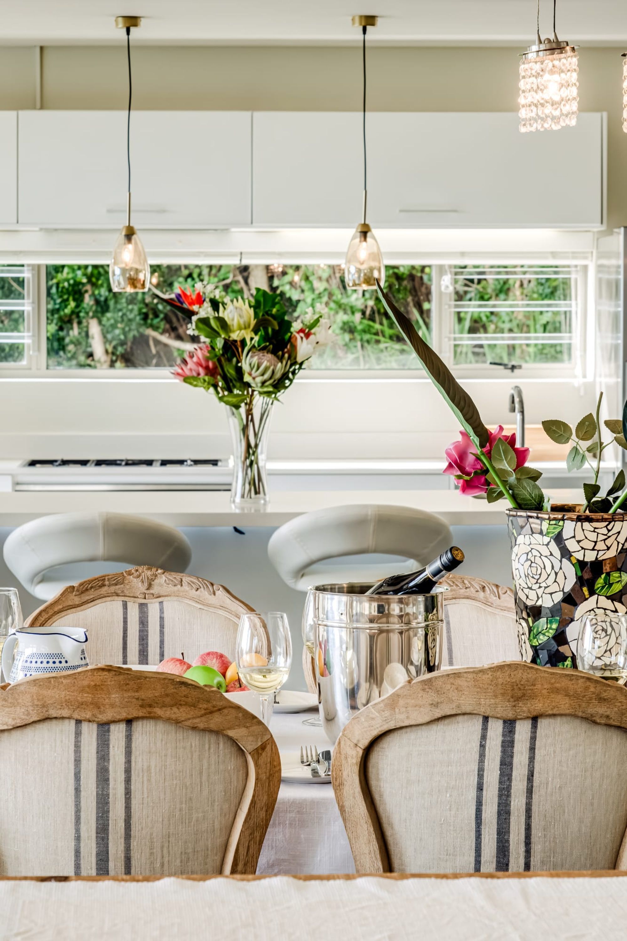 A dining area with a table set for four, a vase with flowers, and hanging pendant lights.
