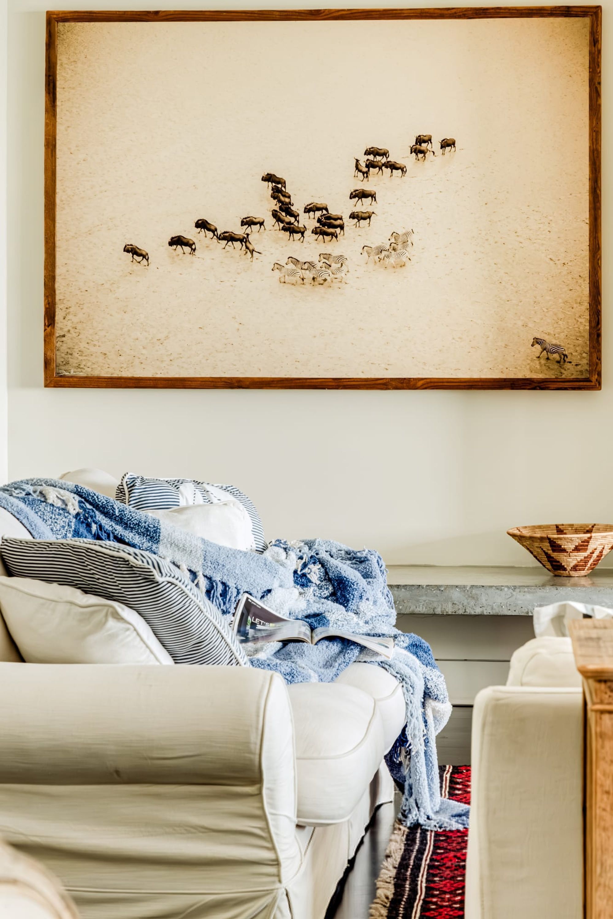 A living room with a large framed artwork of wildlife, a sofa with a blue and white throw, and a wooden side table.