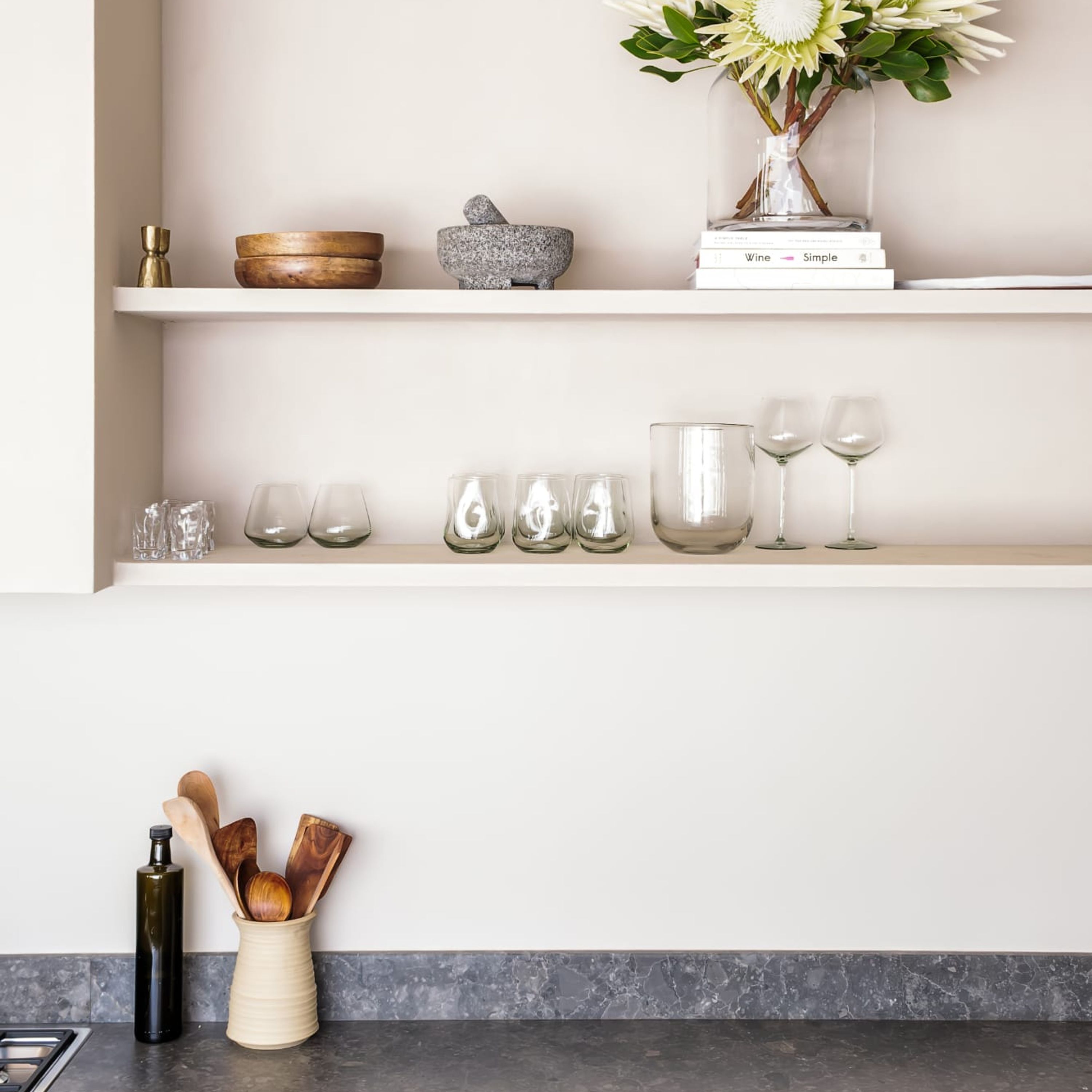 A kitchen shelf with various glassware, a book titled "Wine Simple," and a vase with flowers.