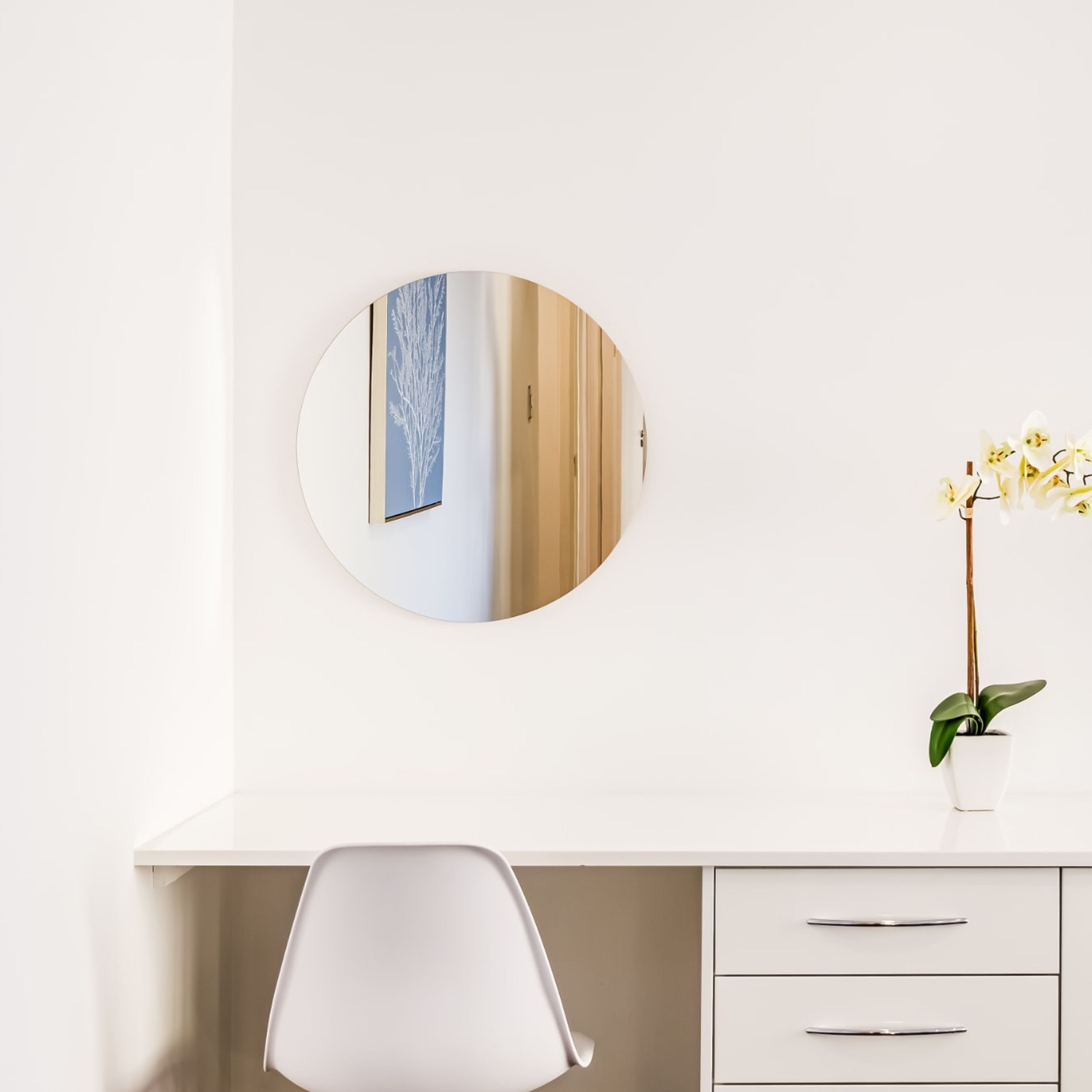 A white desk with a round mirror, a small potted plant, and a chair.