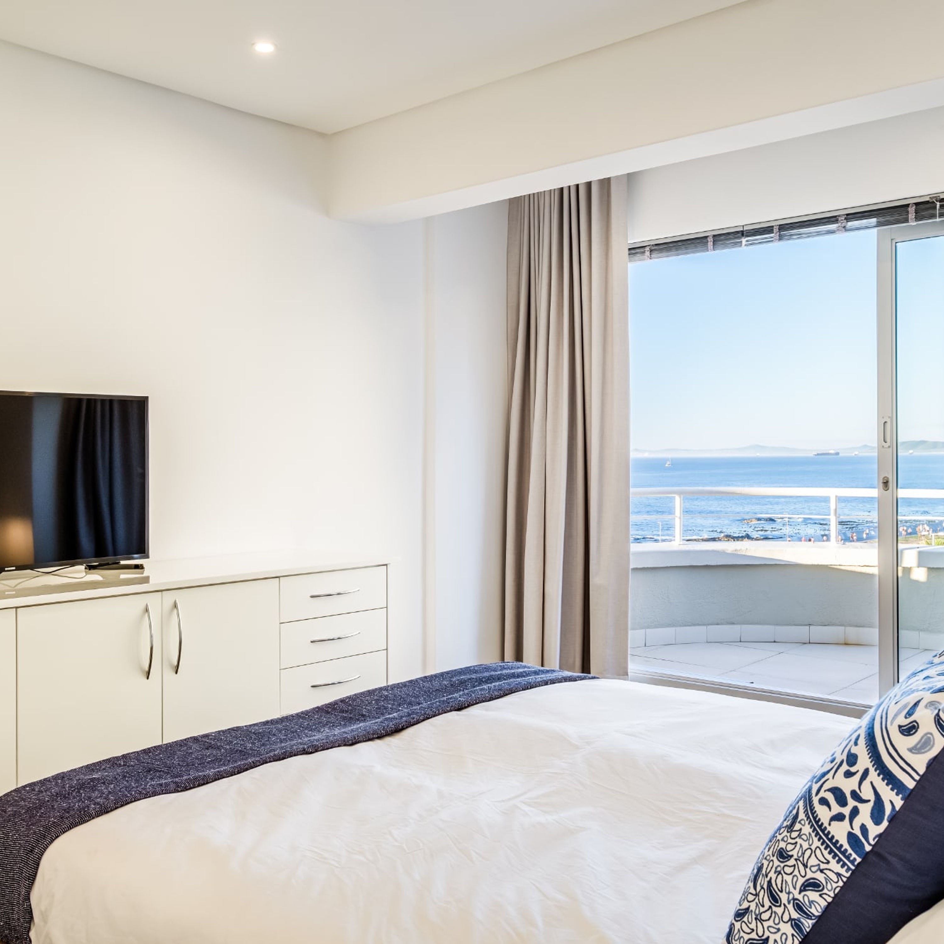 Habitación de hotel con cama, televisión y puerta corrediza al balcón con vista al mar.