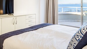 Et hotelværelse med seng, fjernsyn og skydedør til balkon med havudsigt.