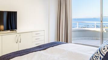 Habitación de hotel con cama, televisión y puerta corrediza al balcón con vista al mar.