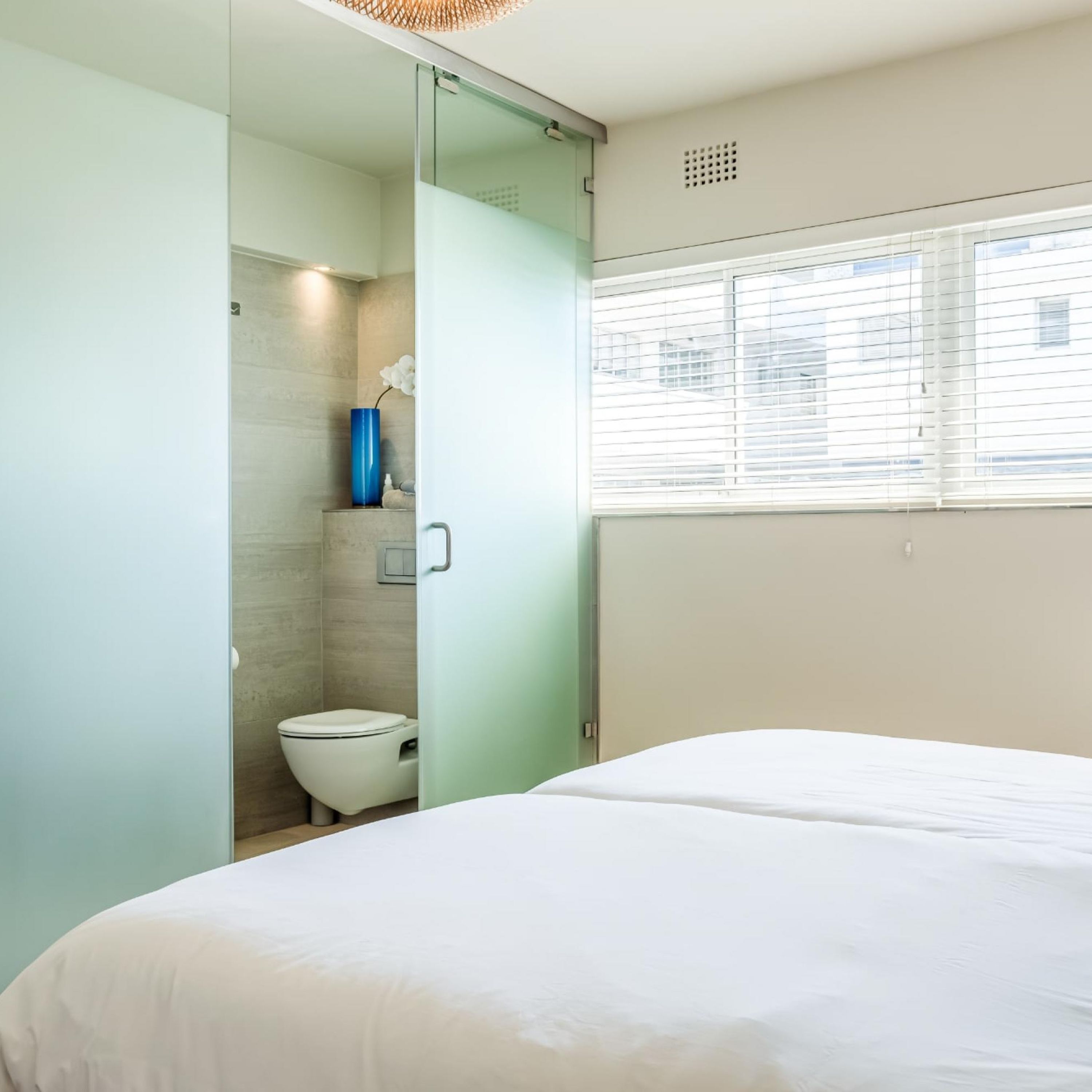 A modern bedroom with a bed, a bathroom with a toilet, and a window with blinds.