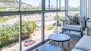 A balcony with large windows offering a view of a cityscape and a mountain.