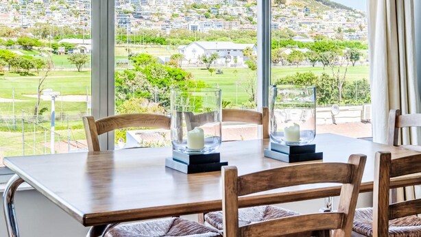 A dining area with a table and chairs, large windows with a view of a hillside and buildings.