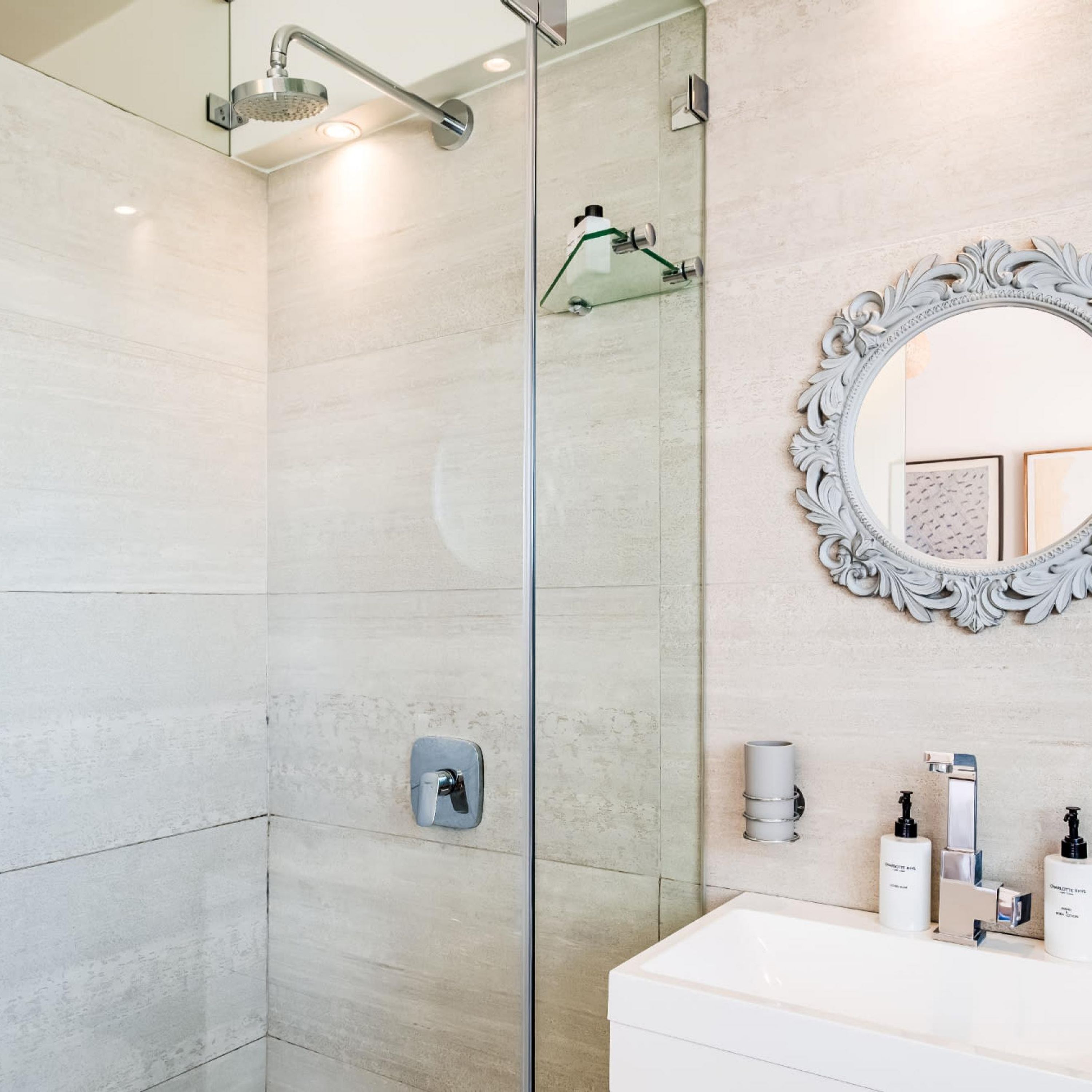A modern bathroom with a glass shower enclosure, a white vanity with toiletries, and a decorative mirror.