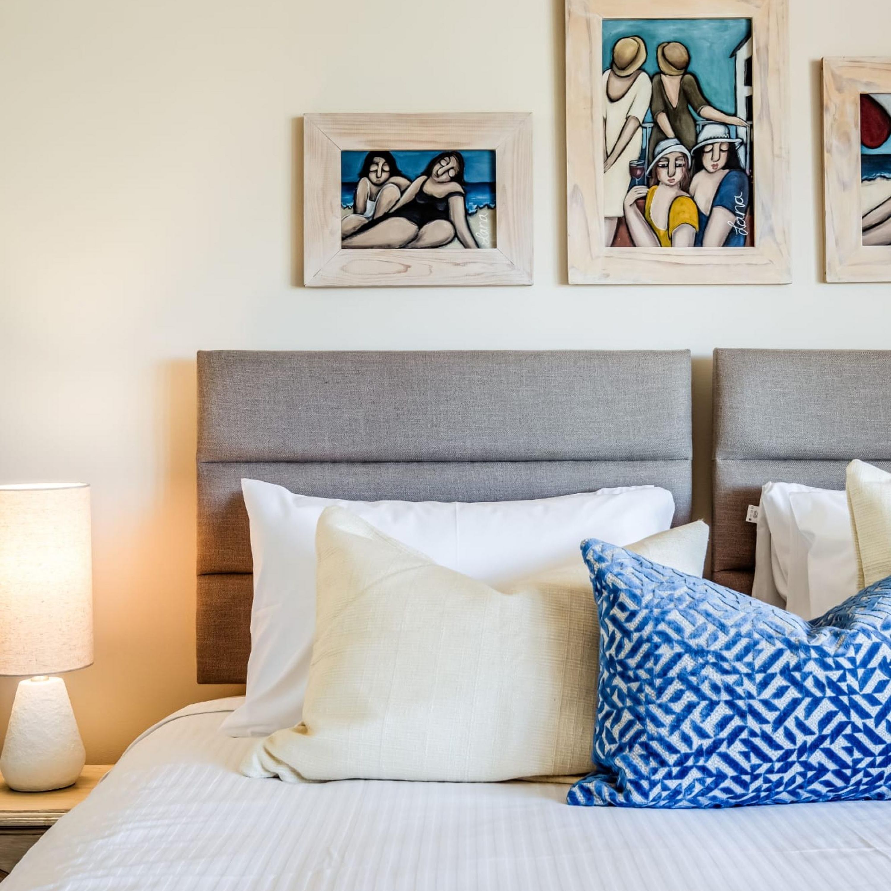 A hotel room with a grey headboard, white bedding, and a lamp on the nightstand.
