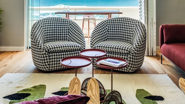 A modern living room with a view of the beach, featuring two houndstooth patterned chairs, a red sofa, and a small coffee table. - Picturesque Seaside Haven Aretzi (Cape Town)
