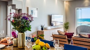 A modern dining area with a wooden table set for a meal, a bowl of fruit, and a vase of flowers. - Picturesque Seaside Haven Aretzi (Cape Town)
