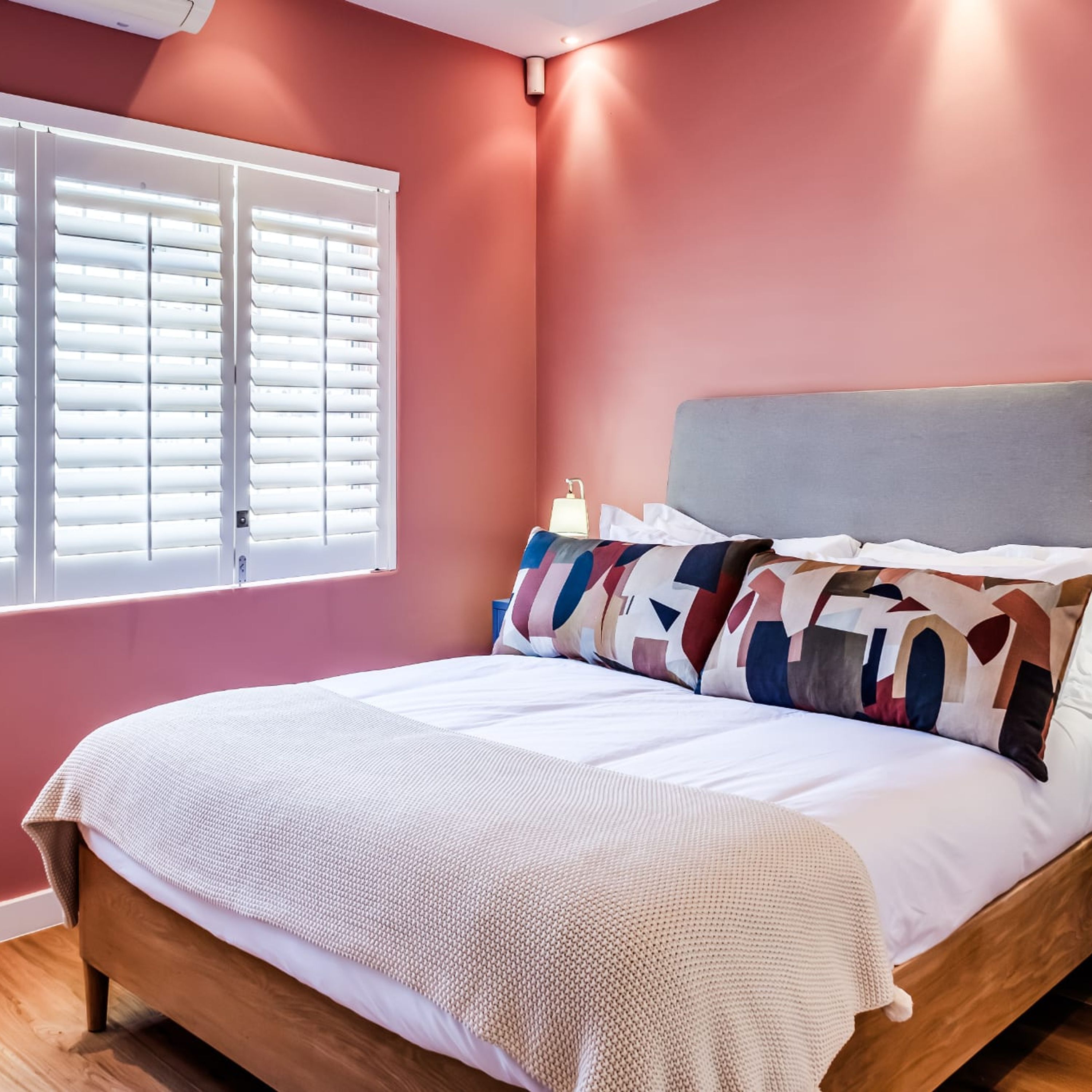 Une chambre à coucher avec un lit, des oreillers, une table de chevet et une fenêtre avec des stores.
