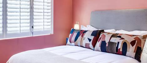 Une chambre à coucher avec un lit, des oreillers, une table de chevet et une fenêtre avec des stores.