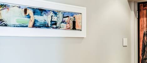 Een gang met een groot abstract schilderij aan de muur en een houten deur.