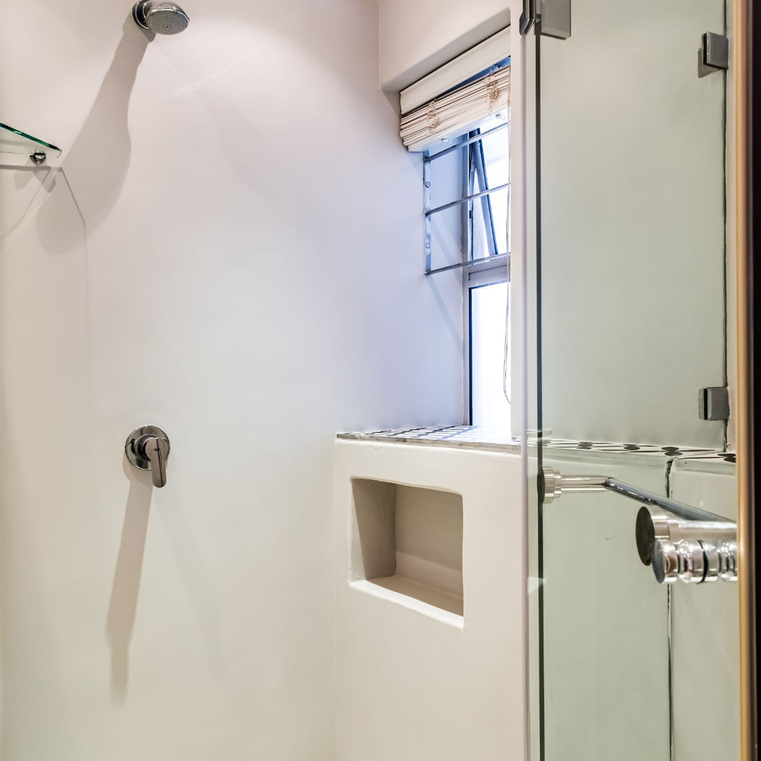 A modern bathroom with a glass shower enclosure, a built-in sink, and a window with blinds.