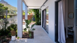 A modern hotel corridor with a view of a mountain, a covered outdoor area with plants, and a room with a bed and a wheelchair. - Elegant Charm Retreat Central Treasure (Cape Town)