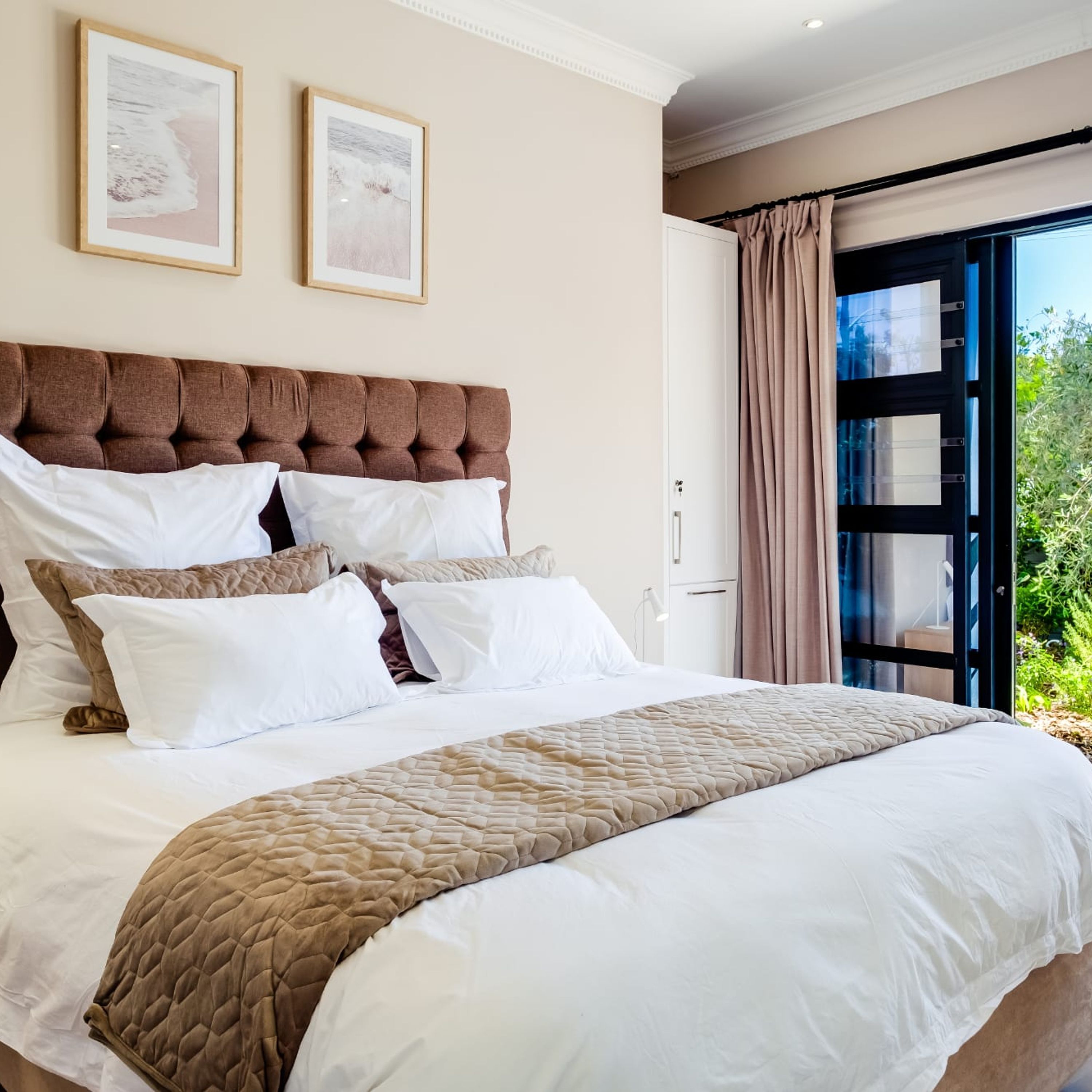 A bedroom with a large bed, two framed pictures on the wall, and a view through a glass door.