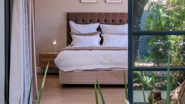 A bedroom with a large bed, a nightstand, and a window with a view of greenery. - Elegant Charm Retreat Central Treasure (Cape Town)
