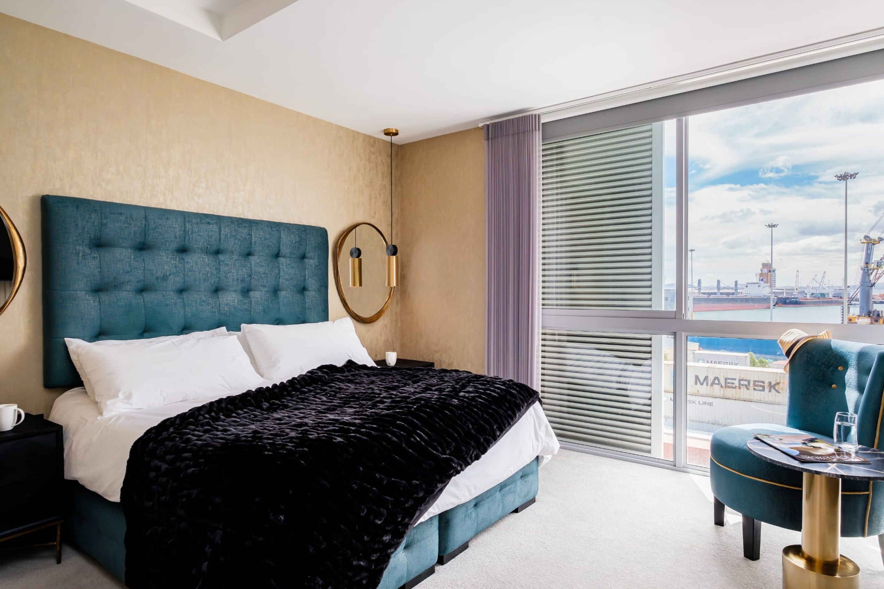 A hotel room with a large bed, a view of the city, and a window with blinds.