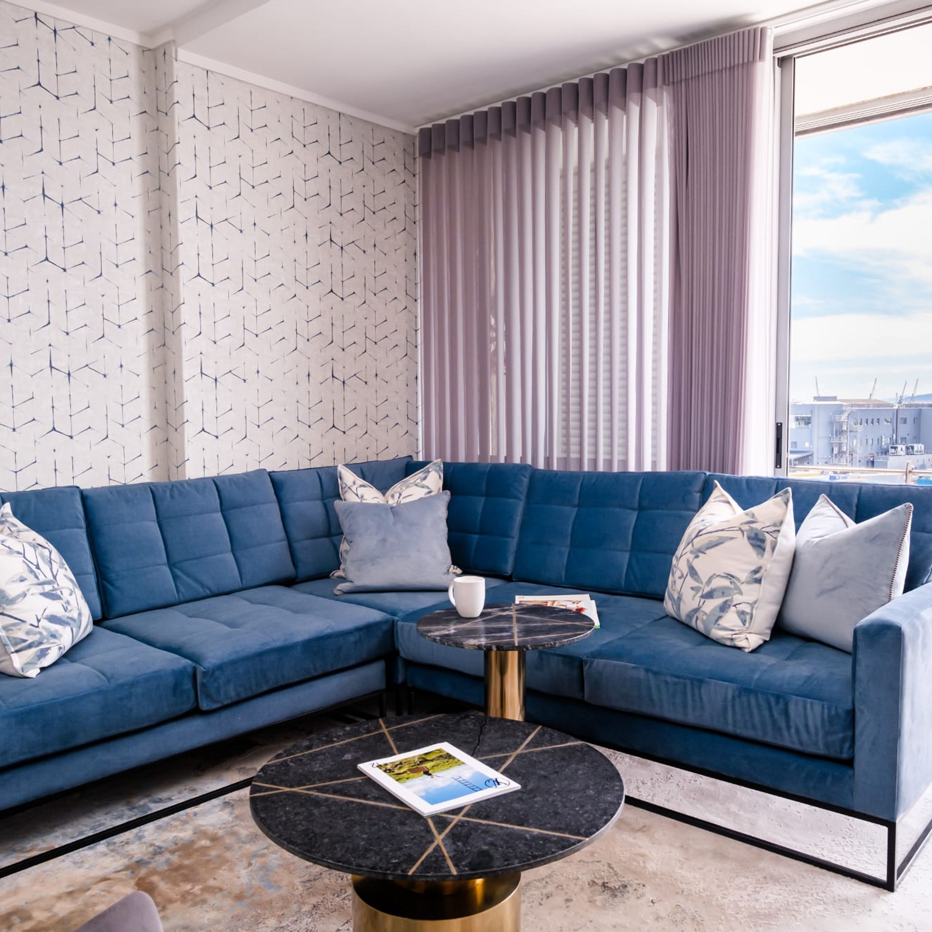 A modern living room with a blue sectional sofa, a round coffee table, and a patterned wall.