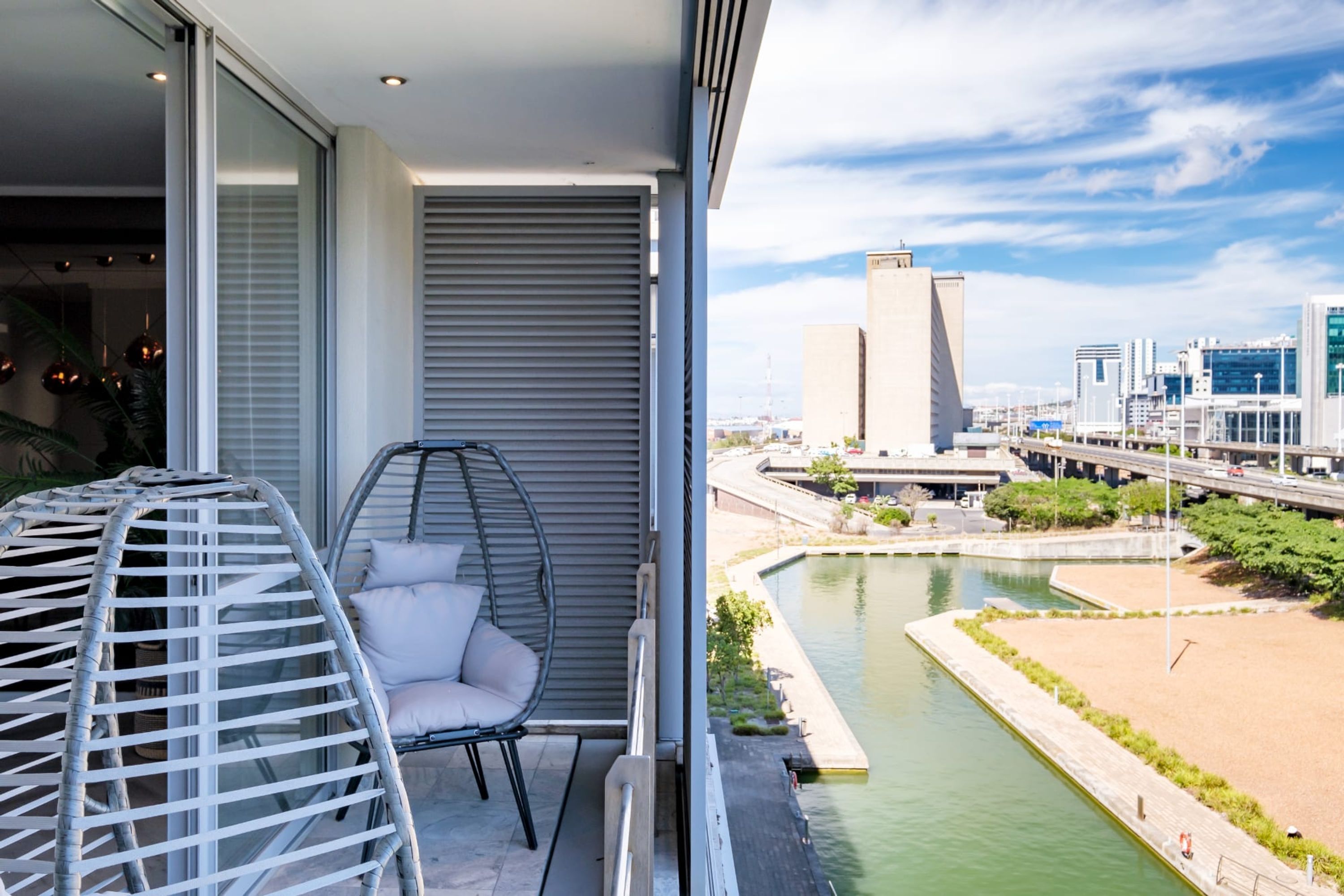 A balcony with a wicker chair and a view of a cityscape and river.