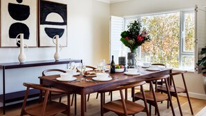 A dining area with a wooden table set for four, a vase with flowers, and abstract art on the wall. - Modern Elegance Meets City Serenity at Meliora (Cape Town)