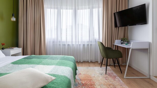 A hotel room with a bed, a desk, a chair, a TV, and a window with curtains. - Holt - Out of the Woods (Bucharest)
